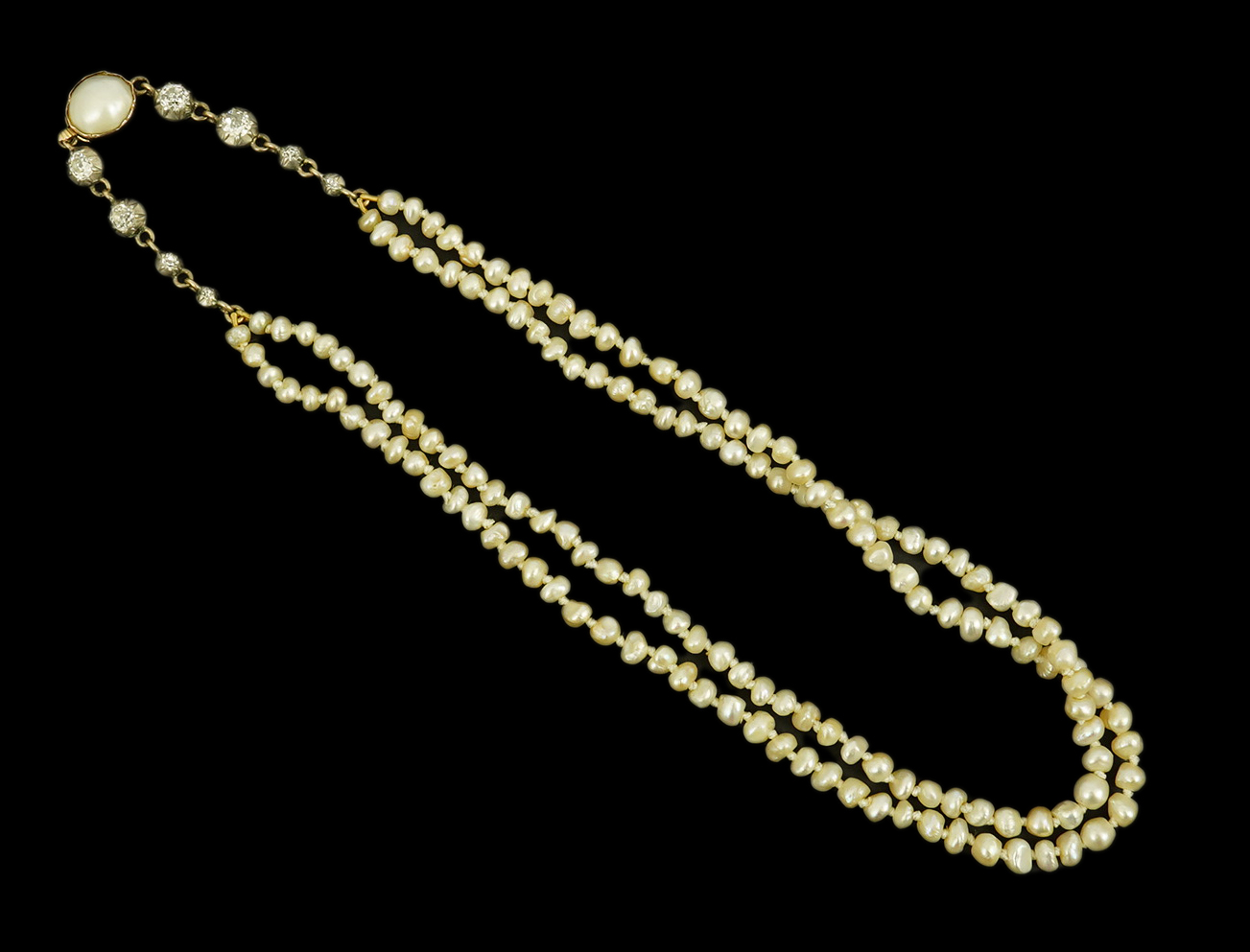 An antique twin strand baroque pearl necklace, with pearl set gold clasp bordered with single chain set with four graduated old mine cut diamonds